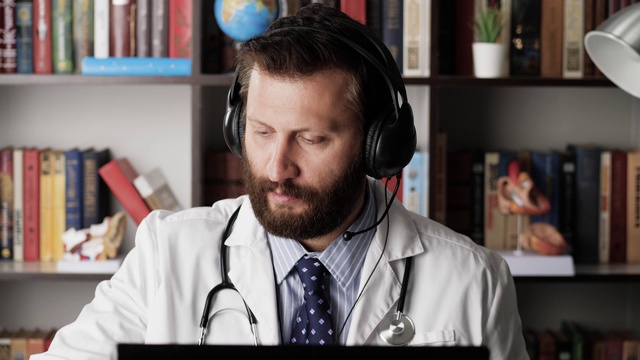 医生的视频电话。男医生在医院办公室工作时戴耳机与病人或同事进行远程视频沟通，倾听并做笔记视频下载
