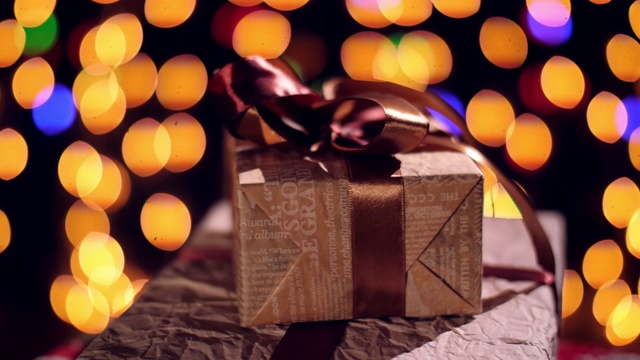 包装精美的巧克力丝带礼物。礼物在散景灯或发光的花环背景。特写,旋转。圣诞节或新年。慈善组织的概念。节日的气氛视频素材