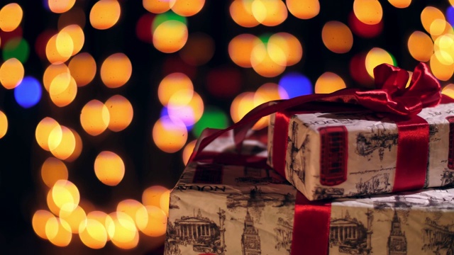 包装精美的礼物用红丝带。礼物在散景灯或发光的花环背景。特写,旋转。圣诞节或新年。慈善组织的概念。节日的气氛视频素材