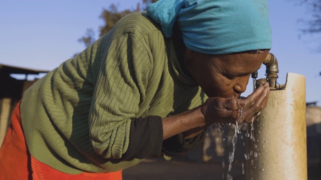 面对贫困。不平等。一个贫穷的非洲黑人妇女的特写镜头，没有自来水，在一个非正式的定居点(寮屋营地)的中央水龙头喝水。视频素材