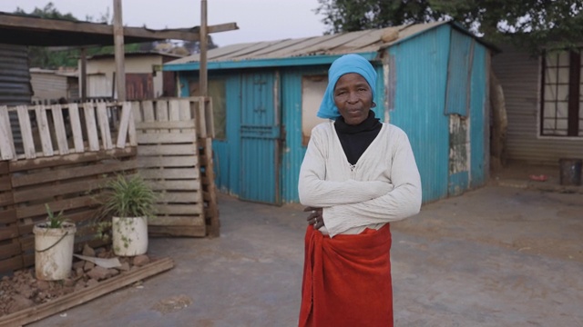 面对贫困。不平等。一个贫穷的非洲黑人妇女站在一个非正式定居点(寮屋营地)密集拥挤和人口稠密的棚屋之间的肖像平移视图。南非视频素材