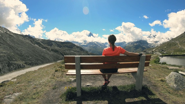 从后面看——女徒步旅行者坐在长凳上休息，欣赏着山的景色视频下载