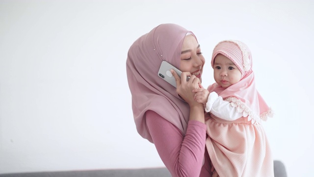 年轻母亲抱着女婴一边讲智能手机视频素材