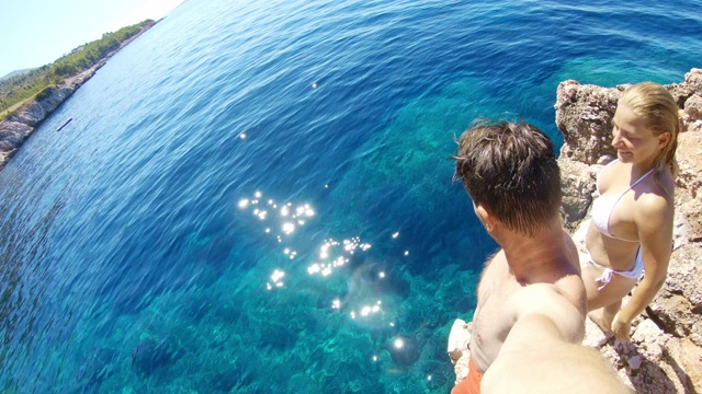 克罗地亚亚得里亚海，一对夫妇带着可穿戴相机跳入阳光明媚的海洋中视频下载