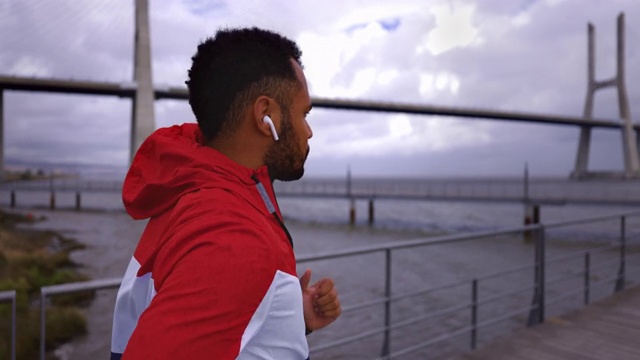 美国黑人戴着耳机在河桥附近奔跑的背影视频下载