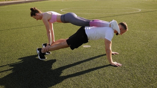 一个年轻人和一个女孩在夏天的户外训练，一个男人在做俯卧撑。视频下载