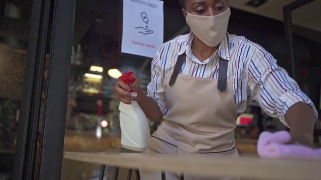 女服务员正在清洁咖啡桌，上面写着“保持社交距离”，用的是强力清洁产品，以便在COVID-19大流行期间对所有东西进行消毒视频下载