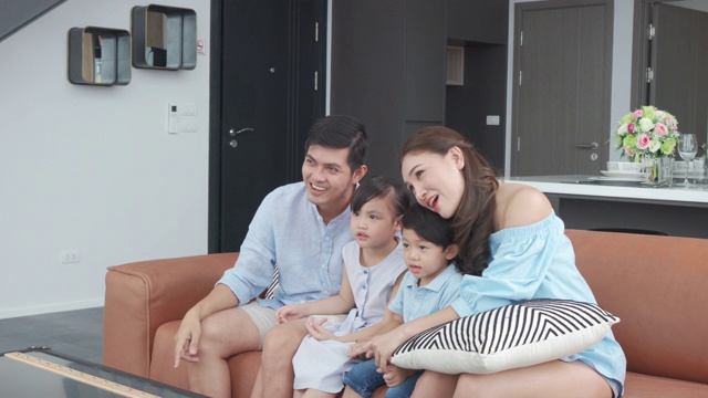亚洲幸福家庭坐在家里的客厅看电视，一起度过有质量的时间活动在假期，假日，幸福或生活方式的概念。视频素材