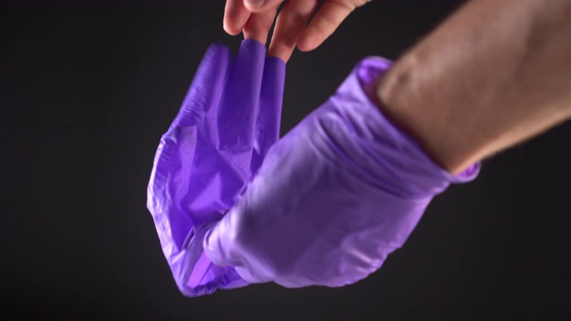 一个男人从两只手上摘下了蓝色的防护手套。在黑色的背景上视频下载