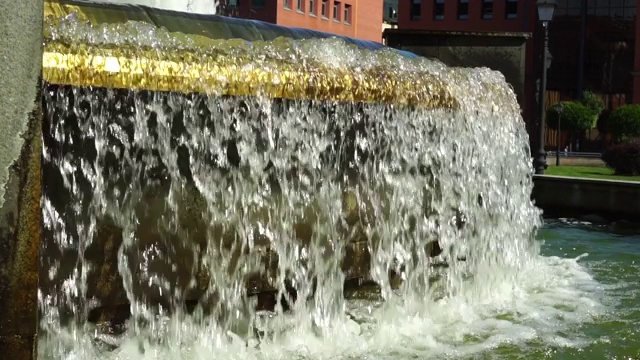 在一个阳光明媚的日子里，一股水流溢出喷泉的金色屏障。视频素材