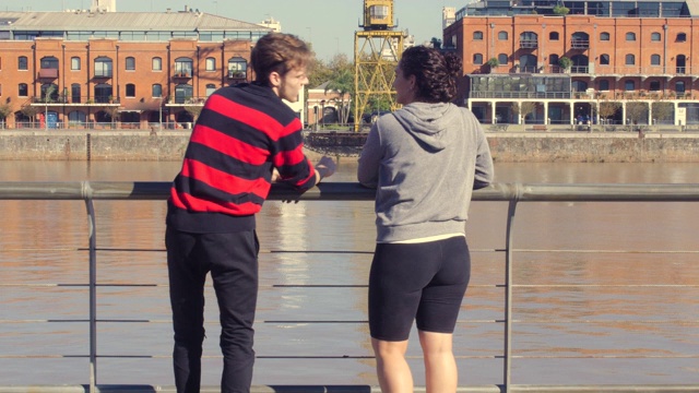 快乐的年轻夫妇轮滑在滨水区公园河边聊天视频下载