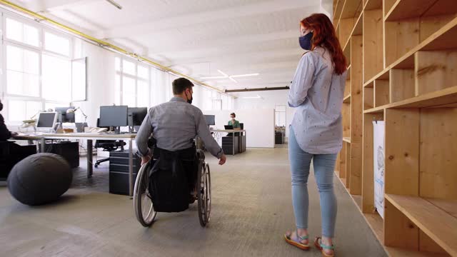 一位坐轮椅的商人和一位女同事一起走进办公室视频下载