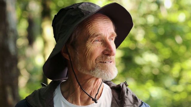 一个戴着帽子站在森林里看相机的老人的肖像视频下载