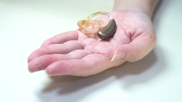 一名妇女的左手掌中有一个助听器。手的特写，背景是白色的。视频下载