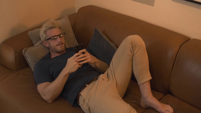 男人晚上躺在沙发上看他的手机视频素材