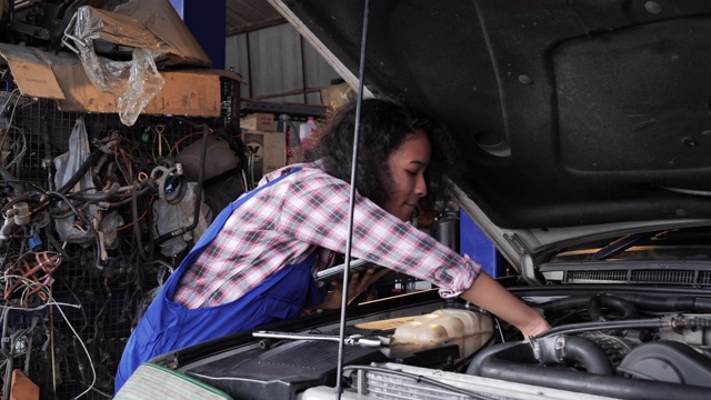 美丽的赋权女机修工是在汽车服务工作的一辆车。戴安全眼镜的女人正在进行一项普通的汽车保养。她在用棘轮。现代清洁车间与汽车。视频素材