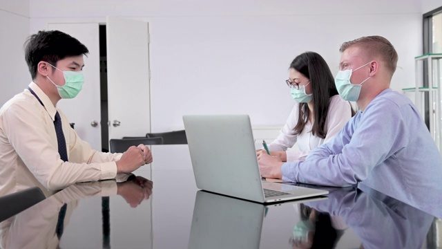 在流感期间，SLO MO经理顾问与亚洲客户在商务会议上使用笔记本电脑，佩戴防护口罩视频下载