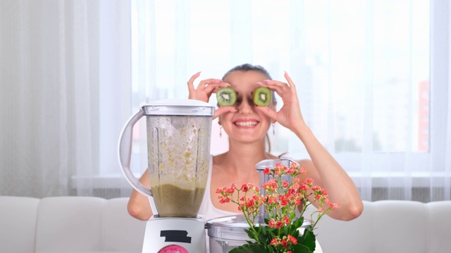 快乐的年轻女子准备美味的营养奶昔在搅拌机。有趣的女性做眼睛从几维视频素材