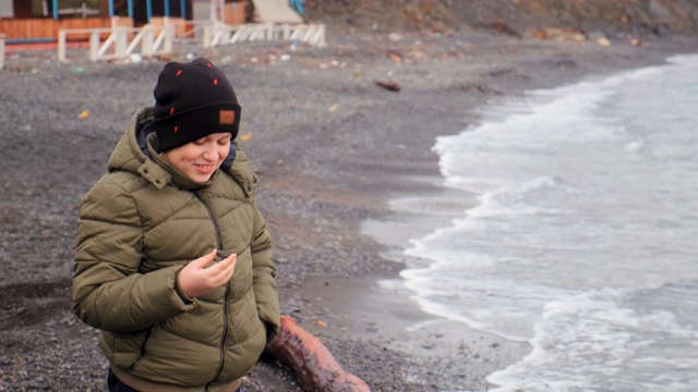微笑的男孩举着石头站在海边的岩石海滩上视频下载