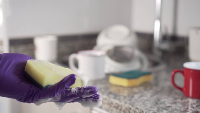 在厨房水槽里一堆没洗过的盘子的背景下，清洁凝胶从上面流淌到黄绿色泡沫海绵上。视频素材