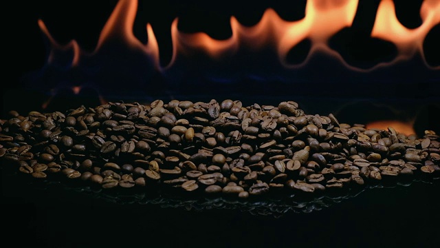 在黑色的背景上用火焰烤咖啡豆。烘焙咖啡的过程视频下载