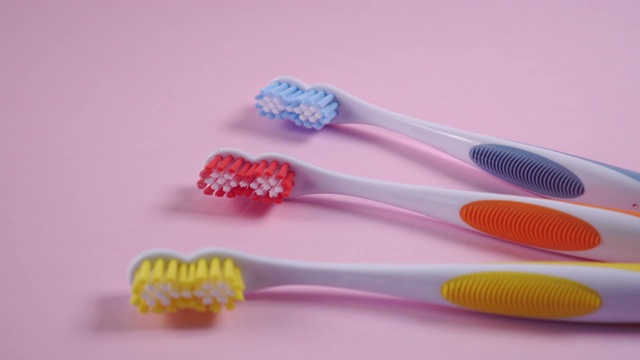 三把亮色的牙刷在精致的粉红色背景上。红色,黄色,蓝色视频下载