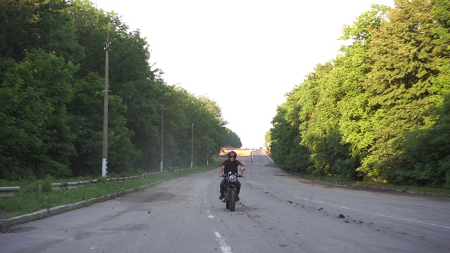 骑摩托车的人在黄昏的乡村公路上飞驰，咖啡车手摩托车冒险的生活方式视频素材