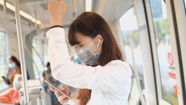 年轻的亚洲女性在捷运中使用智能手机，戴着保护面罩视频素材