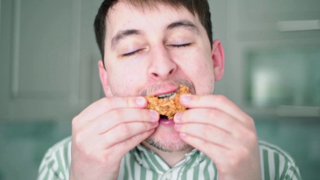 一个人咬了一只鸡翅。过量饮食和肥胖。有害的快餐视频素材