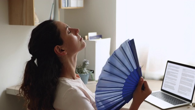 压力大的女人用扇子在家里给自己降温视频素材