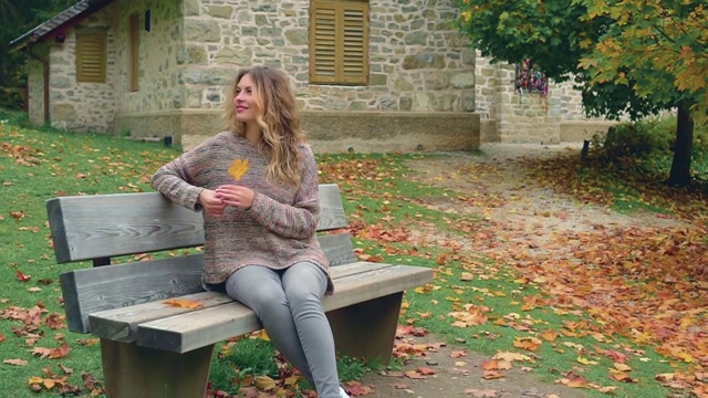 快乐的女人毛衣坐在木凳上，手里拿着枫桔叶视频下载