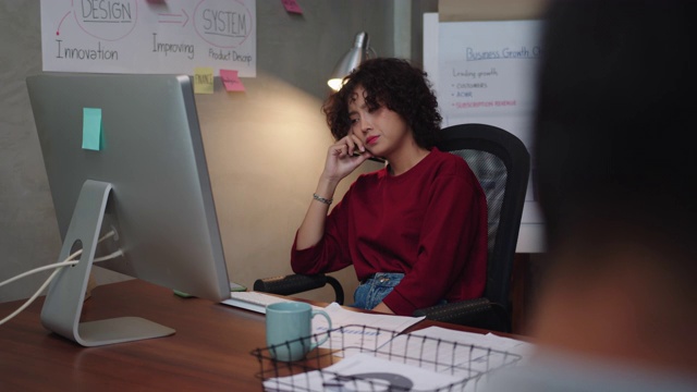 严肃的年轻亚洲女商人穿着休闲服装在台式电脑上工作思考解决一个问题在办公室工作。在办公室工作到深夜的专注的女人。视频素材