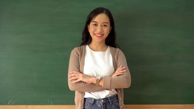 年轻的亚洲女教师在学校教室的黑板前微笑视频下载