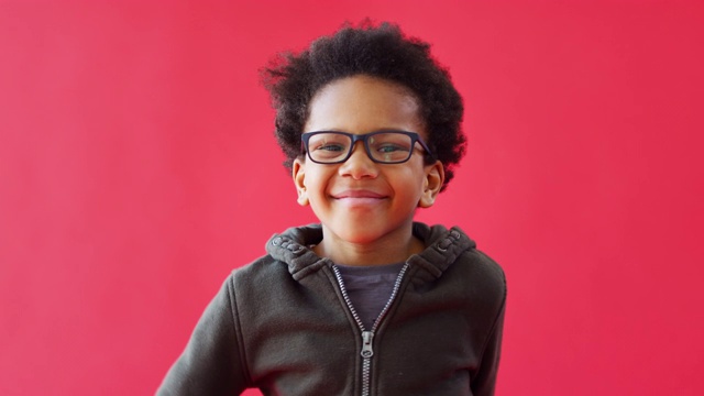戴眼镜的小男孩在红色演播室背景下跳舞，微笑和大笑视频下载