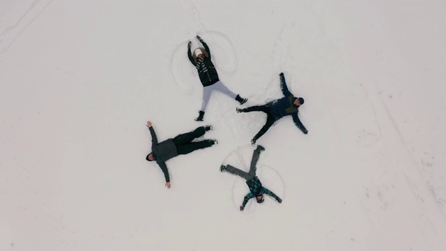 鸟瞰图。一群年轻人把雪天使描绘成躺在新雪上的十字架。四个冬天的天使快乐和精力与雪花飞溅。视频下载