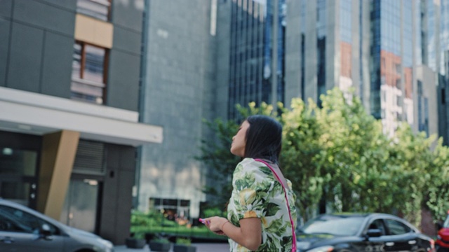 一名亚洲女子在市中心打车。使用手机应用程序视频素材