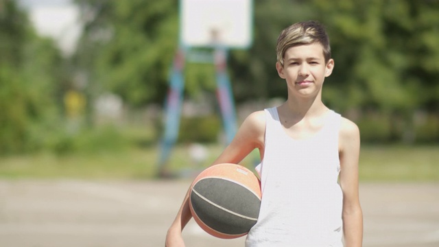 街头篮球场上一个男孩拿着一个球的肖像，光线过饱和视频下载