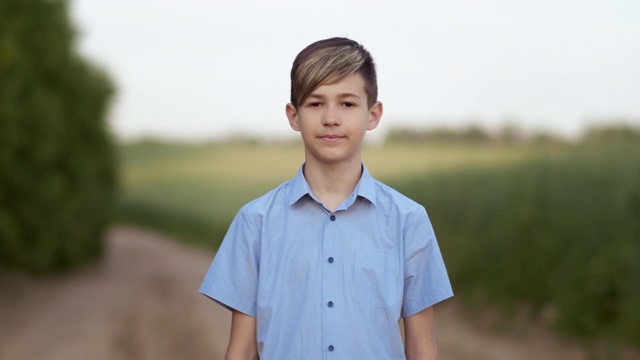 一个快乐的男孩站在自然附近的田野和看相机的肖像视频下载