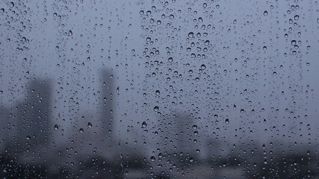 模糊的城市背景下，雨滴落在玻璃窗上。视频素材