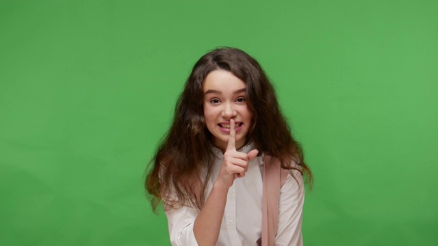 请安静，不要泄露秘密!开朗的十几岁的黑发女孩穿着白衬衫把手指放在嘴唇上，表现出沉默的姿态视频下载