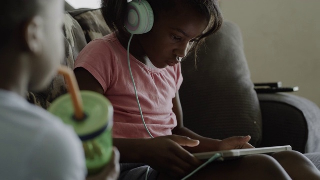 美国犹他州奥勒姆，一名女孩戴着耳机坐在沙发上使用平板电脑，被好奇的哥哥激怒了视频素材