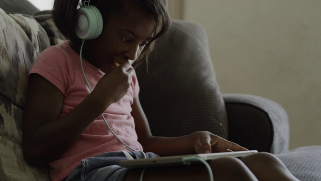 男孩跑来跑去，女孩坐在沙发上戴着耳机使用数字平板电脑/ Orem，美国犹他州视频素材