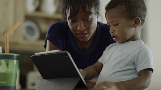 母亲指导微笑的儿子使用数字平板电脑/ Orem，美国犹他州视频素材
