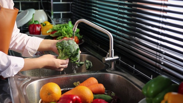 亚洲手妇女洗蔬菜，花椰菜和准备健康的食物在厨房。视频素材