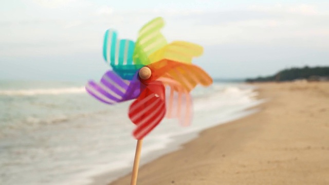 风车旋转着吹着风的塑料风车矗立在海边的沙滩上，映衬着汹涌的海浪。海滩上的玩具。放松。慢动作视频下载