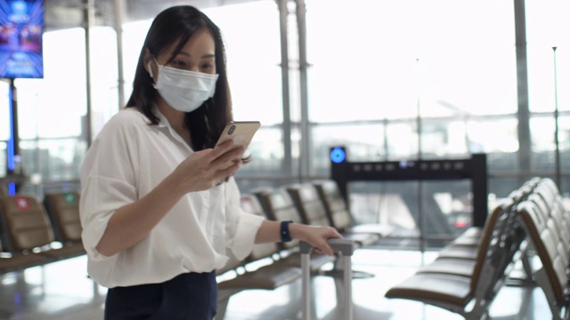 亚洲妇女戴着口罩在机场走路时用手机，慢镜头视频下载