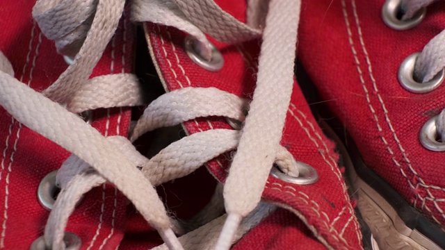 特写旋转一双红色的旧运动鞋匡威与白色鞋带。运动鞋，青春时尚理念。视频下载