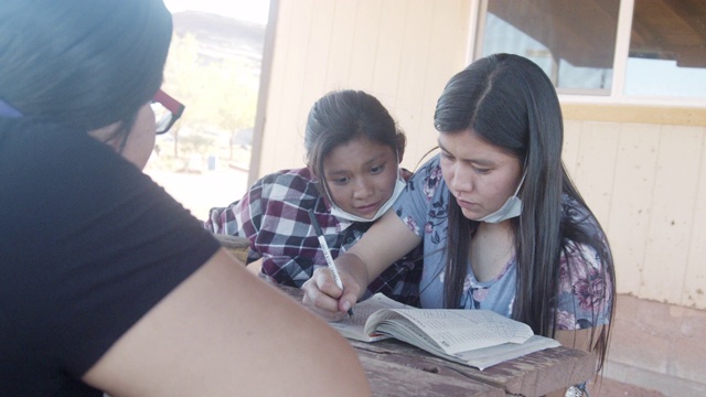 2019冠状病毒大流行期间，美国土著纳瓦霍族的年轻兄弟姐妹们在家门前的户外桌子前一起做家庭作业视频下载