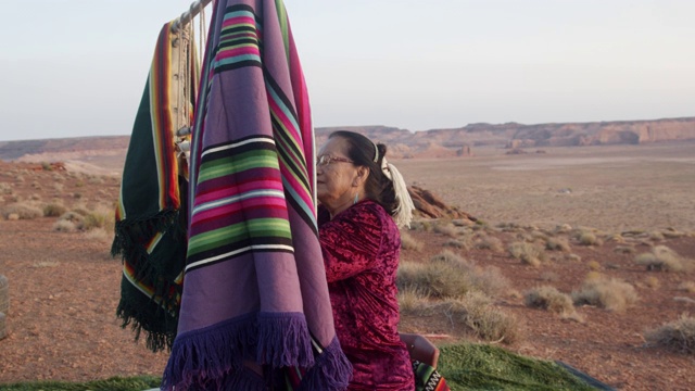 美丽的老年美国土著纳瓦霍妇女在亚利桑那沙漠巨大的纪念碑谷部落公园用老式织布机制作传统印第安毛毯视频素材