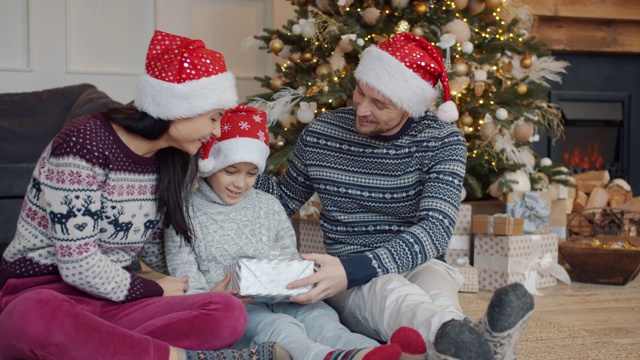 父母戴着新年帽在平安夜在家给快乐的小男孩送礼物视频素材